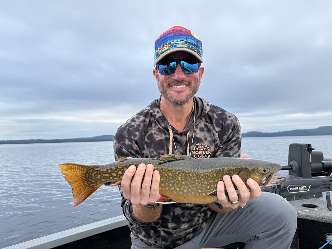 Steve Moore smiling on a boat while holding a large brook trout