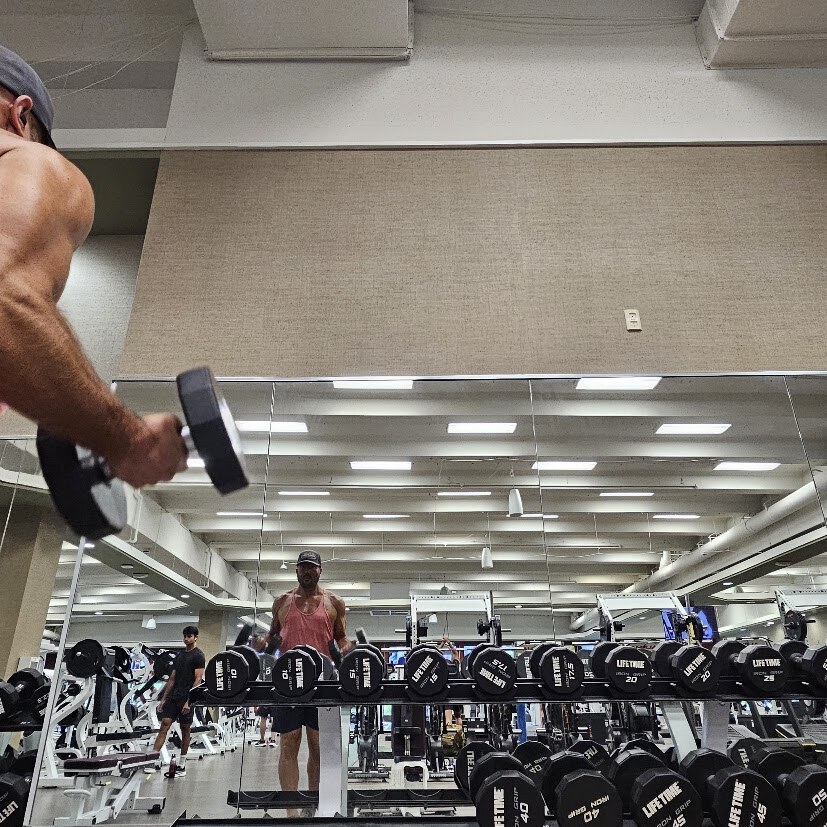 Steve Moore training with dumbbells at the gym, seen in a wall mirror